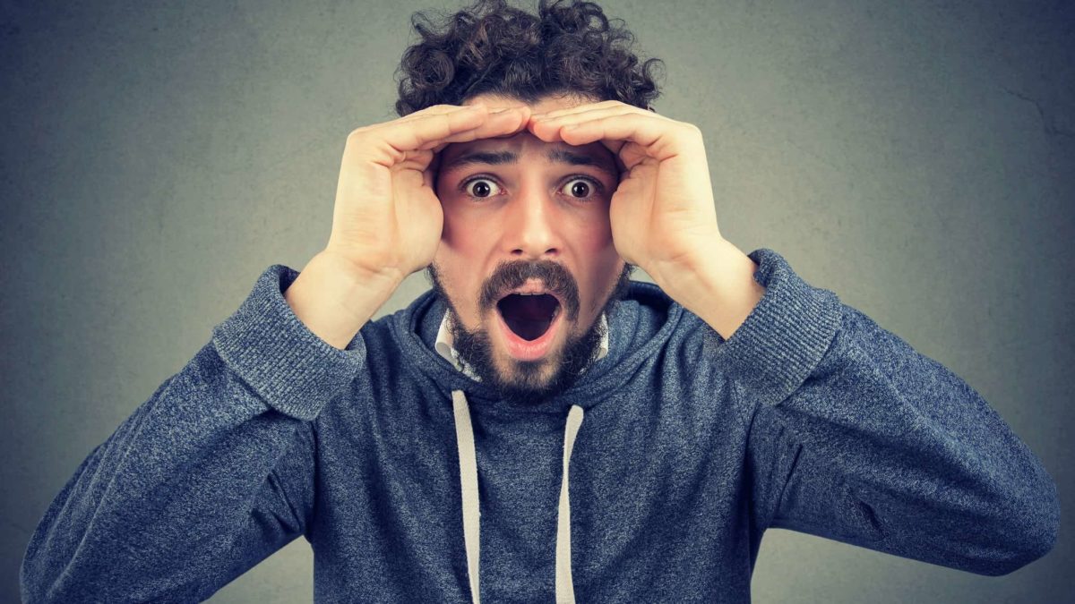 A man peers into the camera looking astonished, indicating a rise or drop in ASX share price