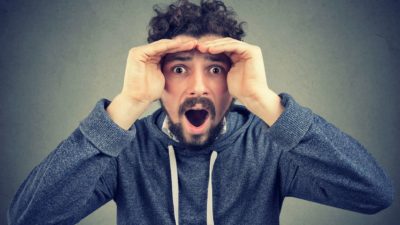 A man peers into the camera looking astonished, indicating a rise or drop in ASX share price