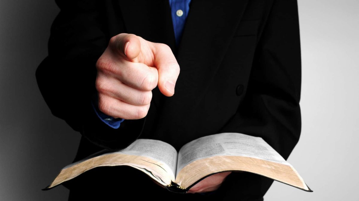 A man holds a law book and points his finger, indicating an accusation or alleged offence to be settled in court