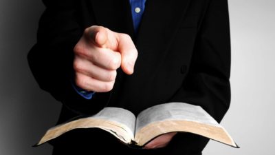 A man holds a law book and points his finger, indicating an accusation or alleged offence to be settled in court