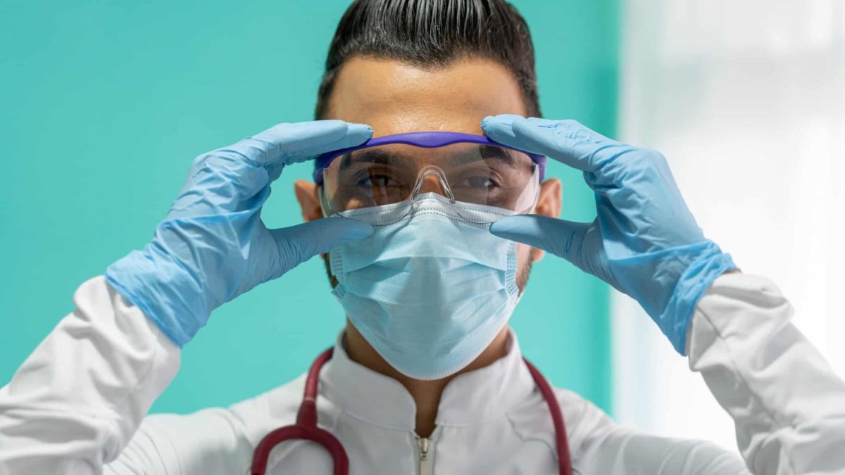 A doctor or medical expert in COVID protection adjusts her glasses, indicating growth or strong share price movement in ASX medical, biotech and health companies
