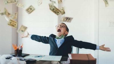 A young entrepreneur boy catching money at his desk, indicating growth in the ASX share price or dividends