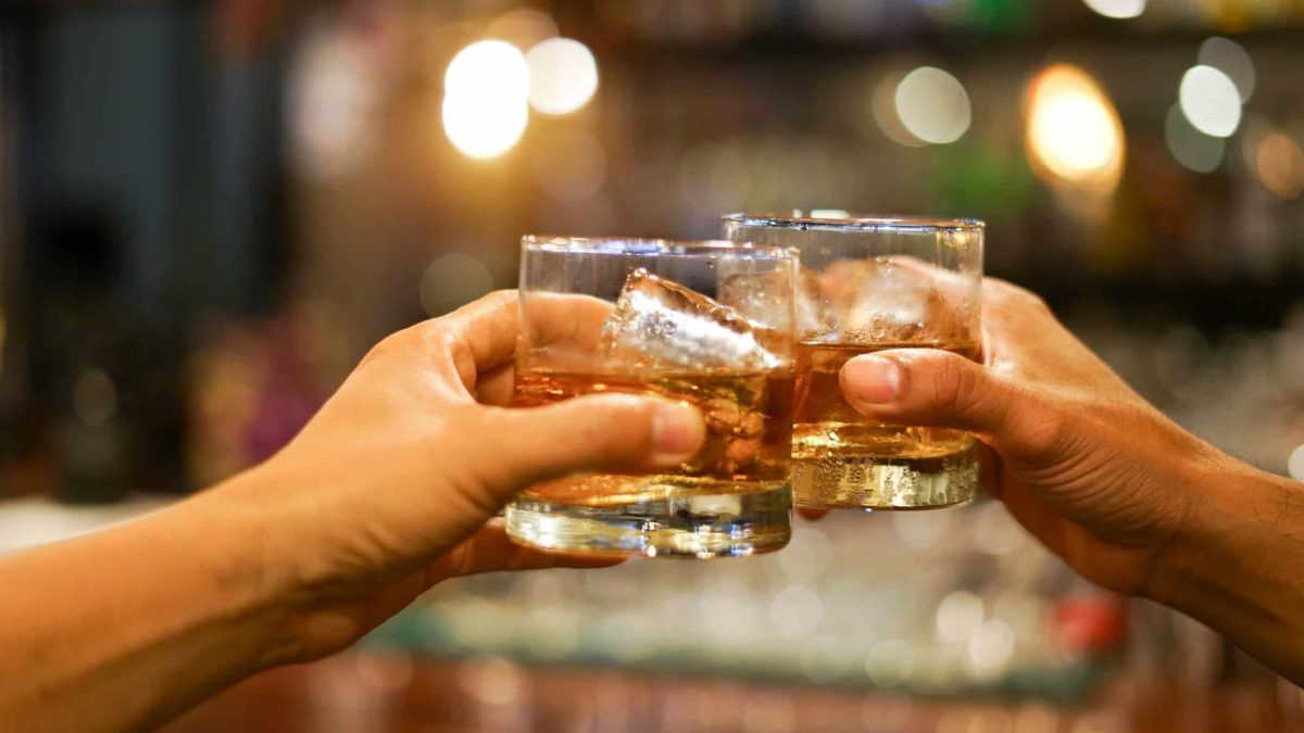 two hands clink together their glasses filled with spirit and ice, indicating a share price rise