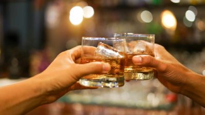 two hands clink together their glasses filled with spirit and ice, indicating a share price rise
