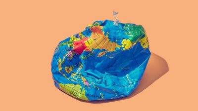 Deflated world globe on peach background to symbolise impact of climate change on the economy