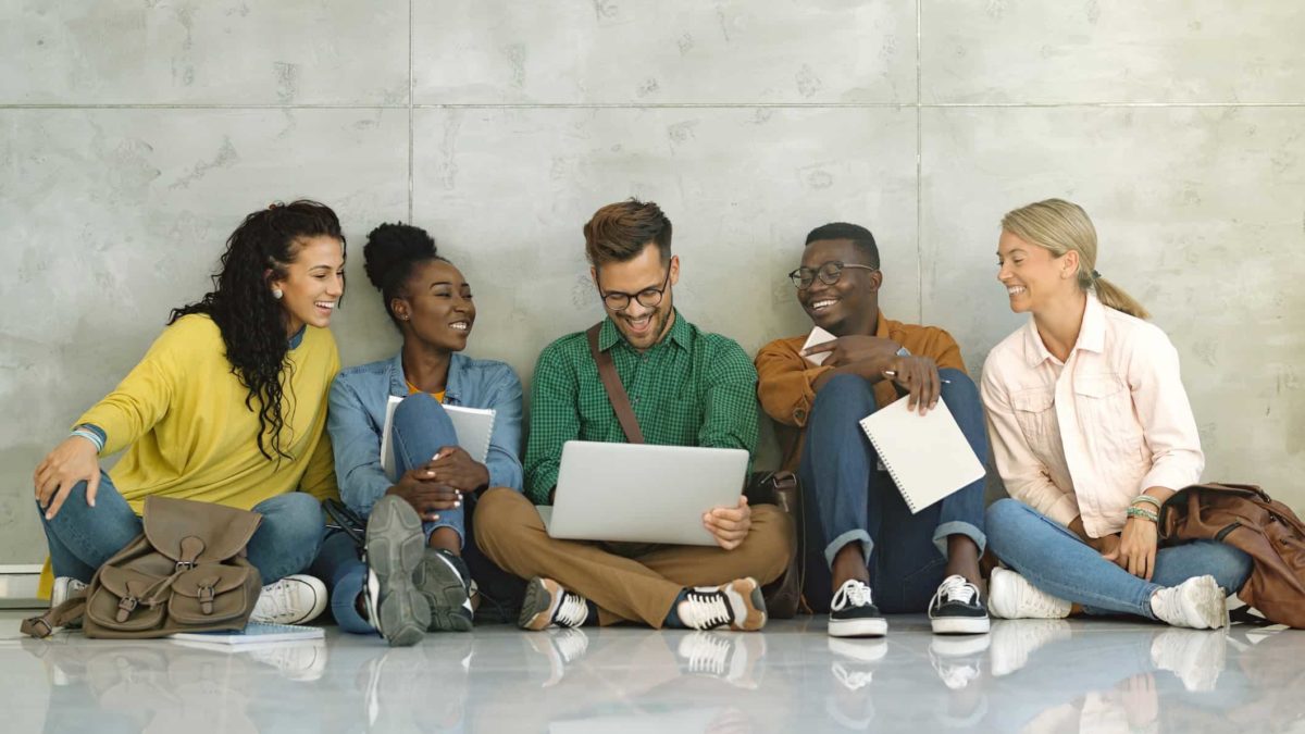 Diverse group of university students smiling and using laptops