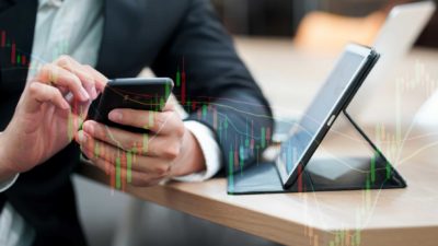 A share market investment manager monitors share price movements on his mobile phone and laptop
