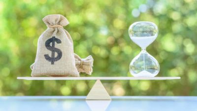 A set of scales with a bag of money balanced against a timer, indicating growth versus value shares