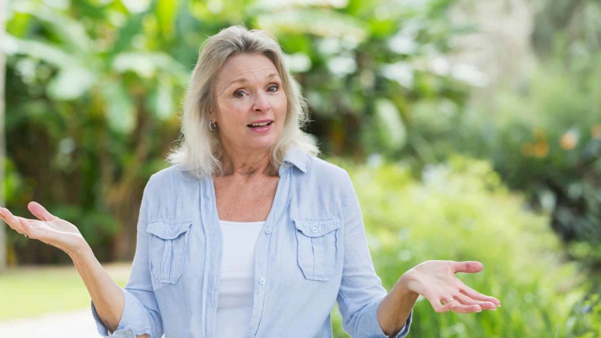 A woman in a green garden shrugs her shoulders, indicating confusion over a company share price