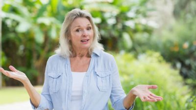 A woman in a green garden shrugs her shoulders, indicating confusion over a company share price