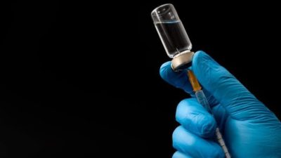 coronavirus vaccine represented by gloved hand drawing down from syringe