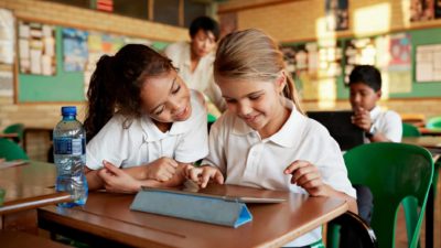 two kids in a classroom using an electronic device