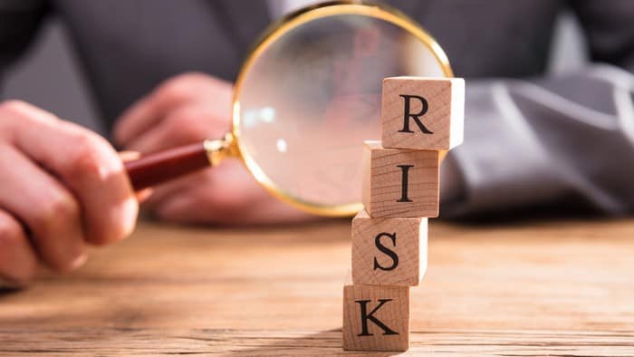 person with a magnifying glass with four blocks of letters spelling out risk on top of each other