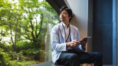Envirosuite investor holds a tech device while sitting on a ledge looking out to trees through a window