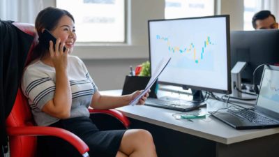 Woman using her mobile phone at her desk with graph on computer