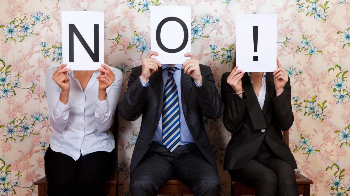 three people in business attire holding up paper signs spelling no