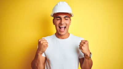 Man in mining hat with fists raised and eyes closed looking happy and excited about the Newcrest share price