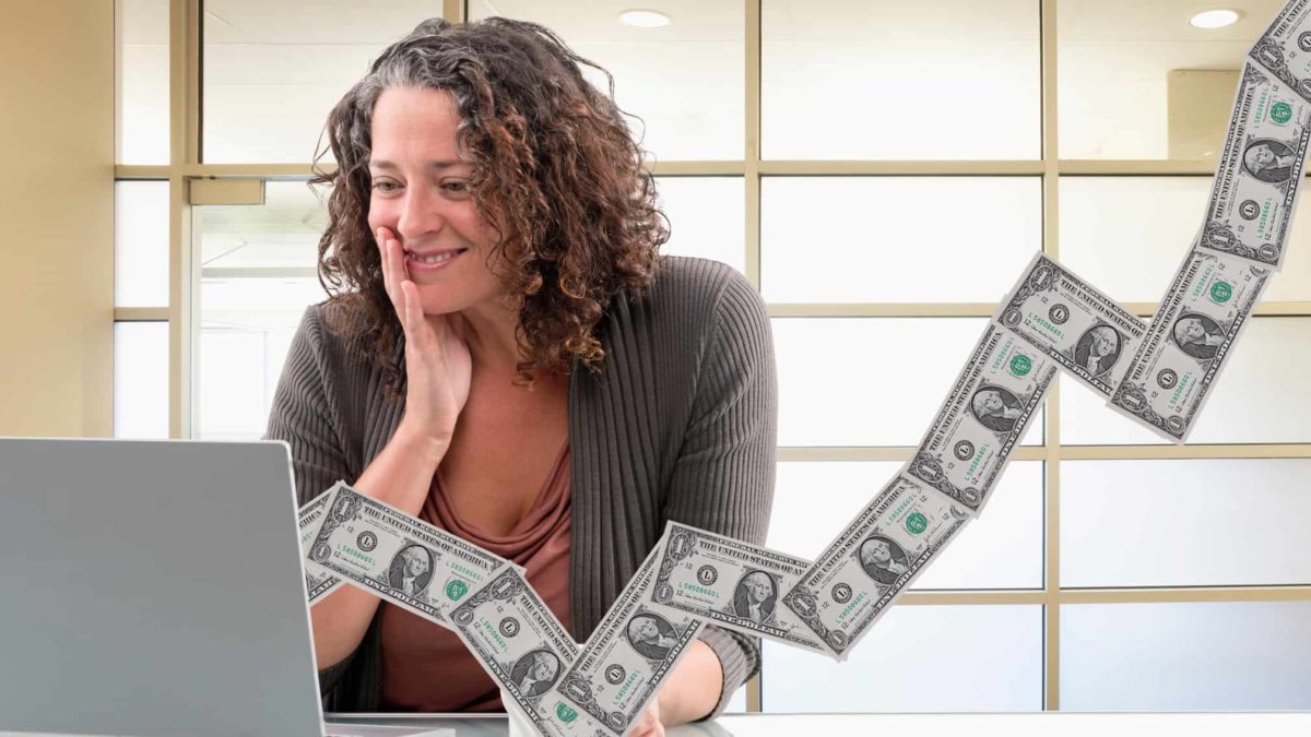 happy woman looking at her laptop with notes of money coming out representing financial success and a rising share price and dividend yield