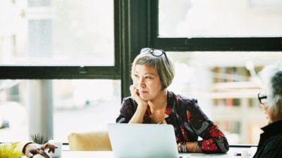 woman sitting down with her laptop open and day dreaming