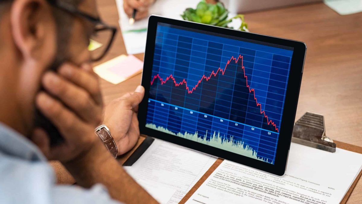 person watching share price fall on device with head resting on hand
