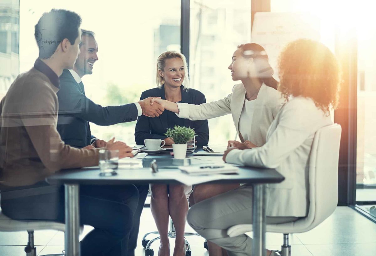 Jumbo Interactive staffers shaking hands around table agreeing to an acquisition