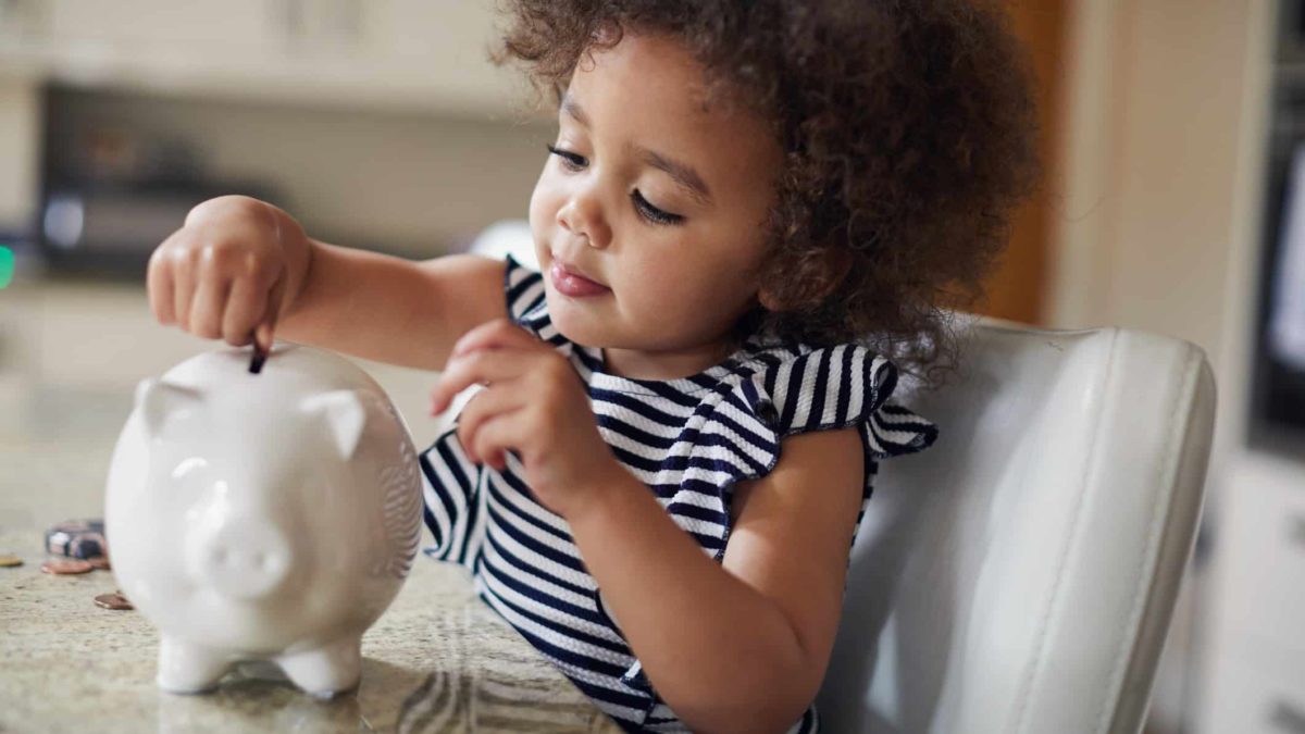Little girl adding money to her piggy bank savings