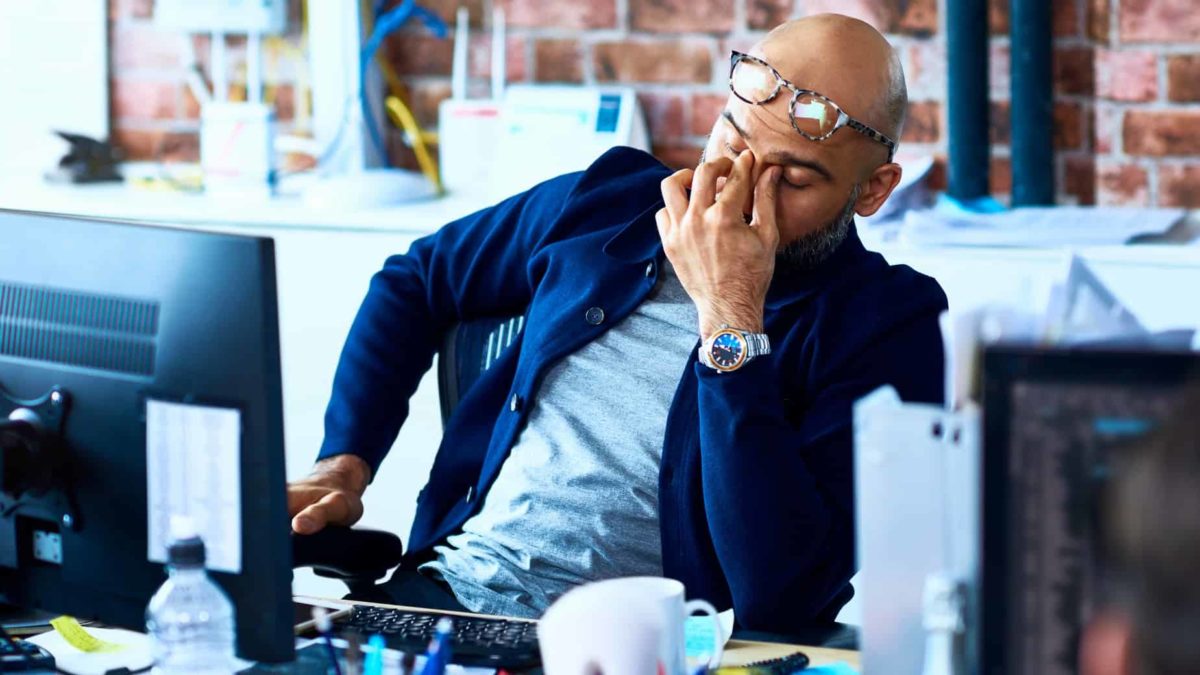A man wearing a suit and sitting at his desk in front of his computer puts his hand to his forehead in frustration over the delayed Afrterpay takeover