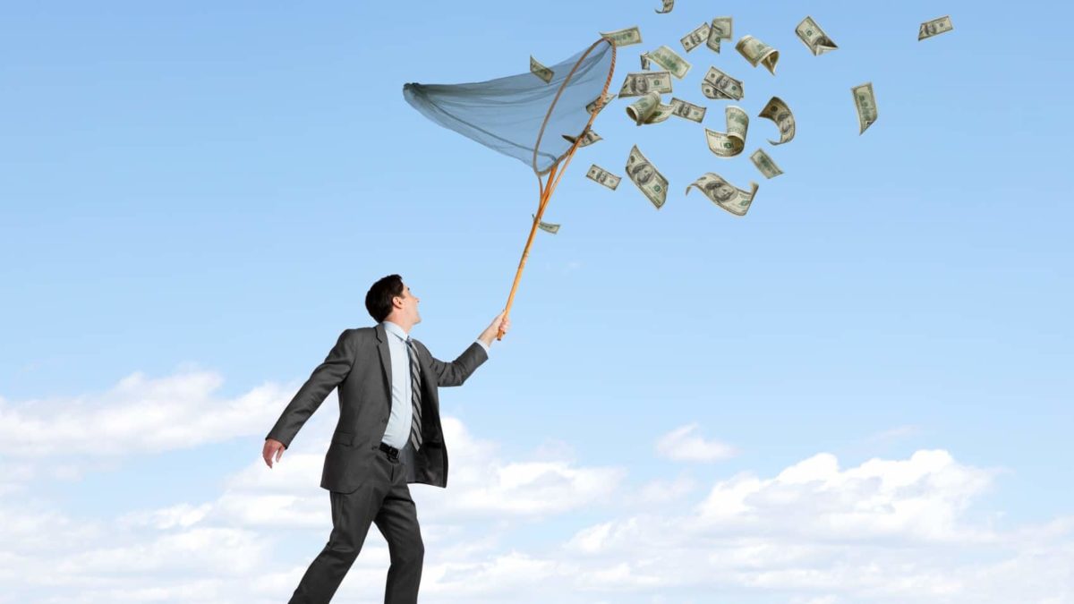 investor holding a net and trying to catch money flying around in the wind.