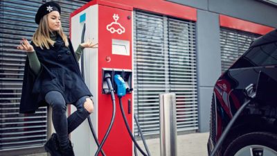 A fashionable girl sitting and waiting whilst charging her electric vehicle.