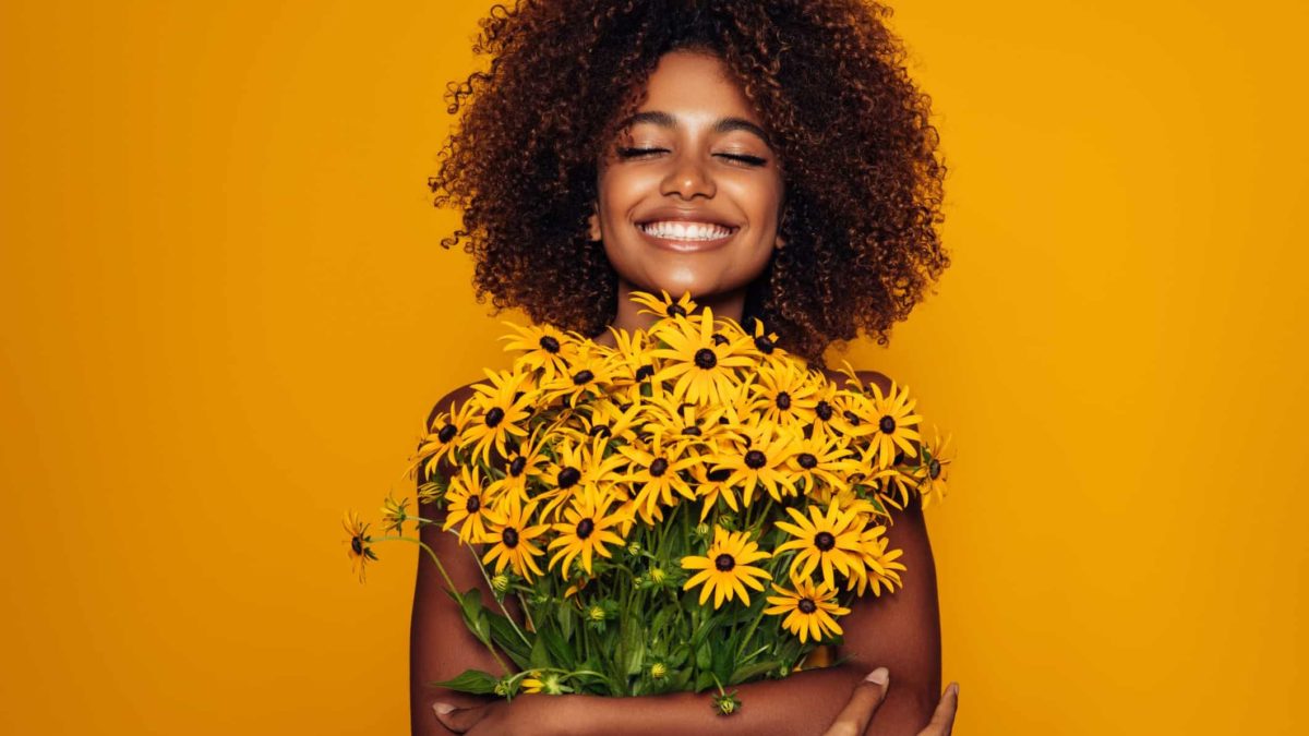 A smiling woman holds a bunch of flowers, indicating growth