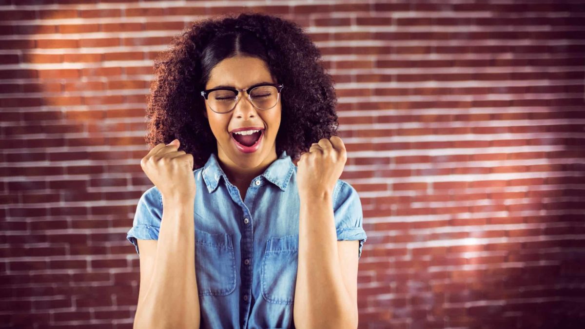 A woman cheers in front of brick wall.