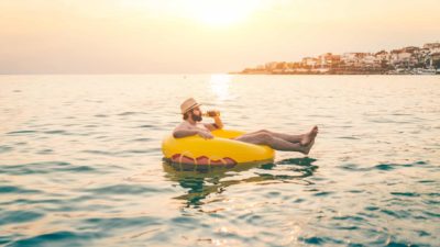 Man drinking from a bottle sitting on a floating ring in the middle of a harbour going nowhere.
