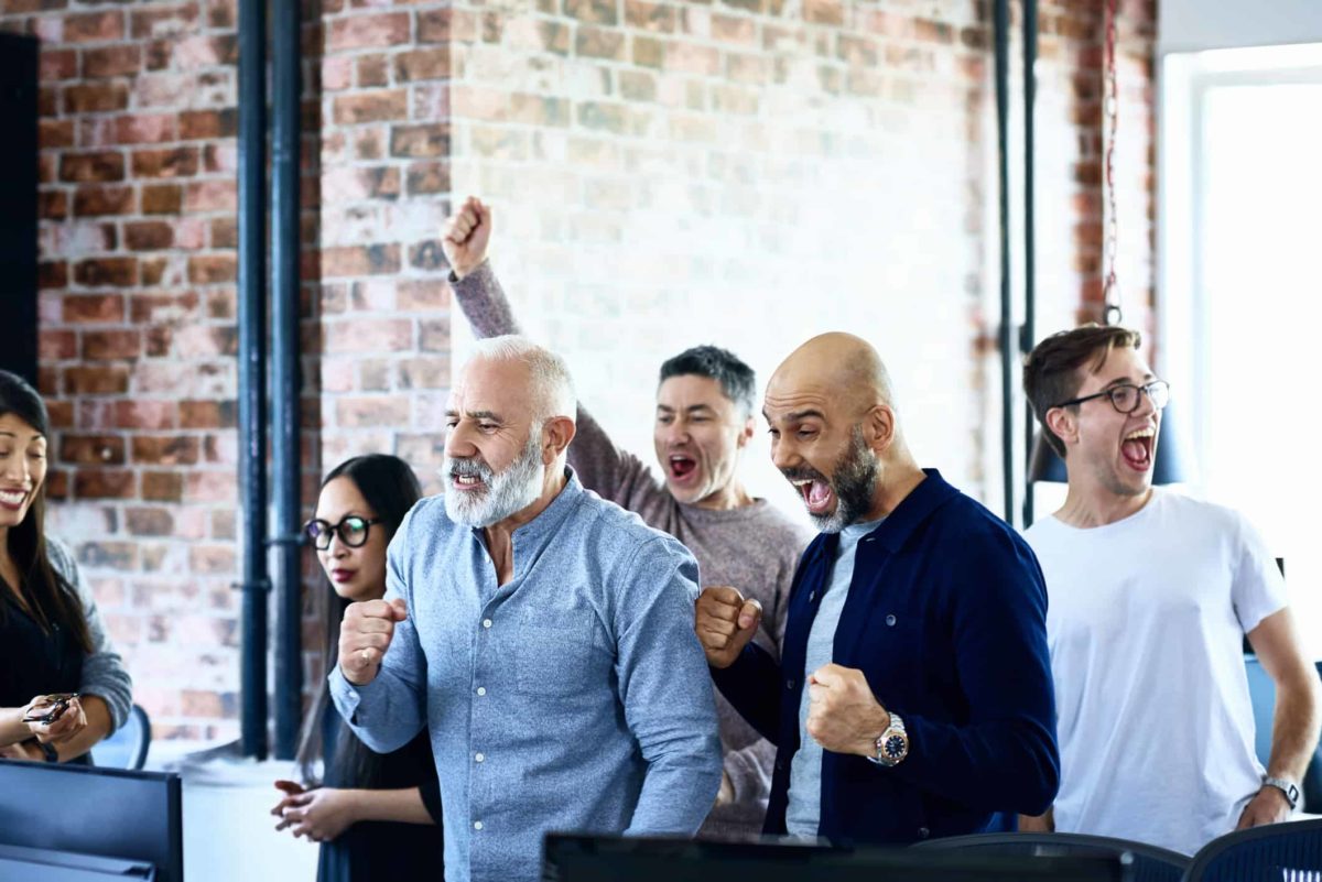Group of six people in a modern office cheering at a computer screen. as the Magnis share price soars on promising battery test results