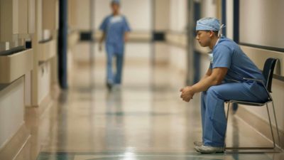 A health professional sits contemplating in the corridor of a hospital.