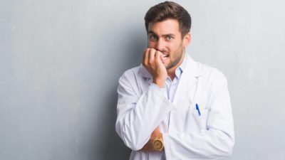 A healthcare worker wearing a white coat holds his fingers to his mouth looking worried as healthcare stocks like Cochlear crash today