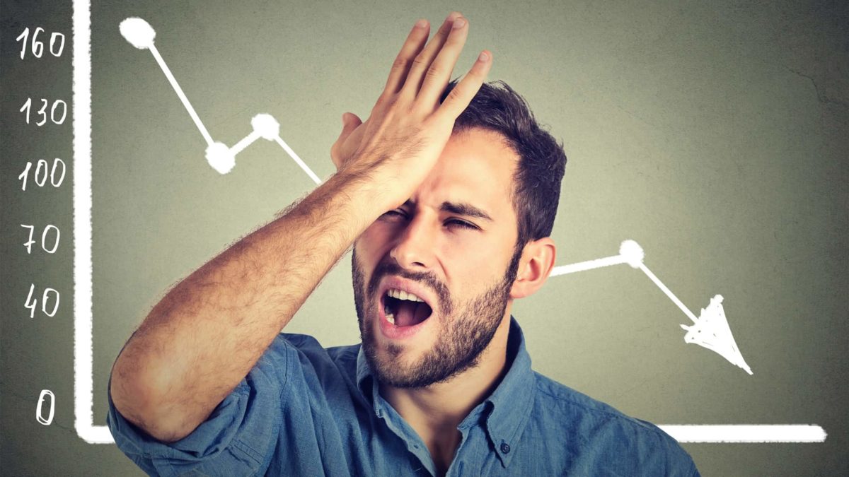 A man stands in front of a chart with an arrow going down and slaps his forehead in frustration.