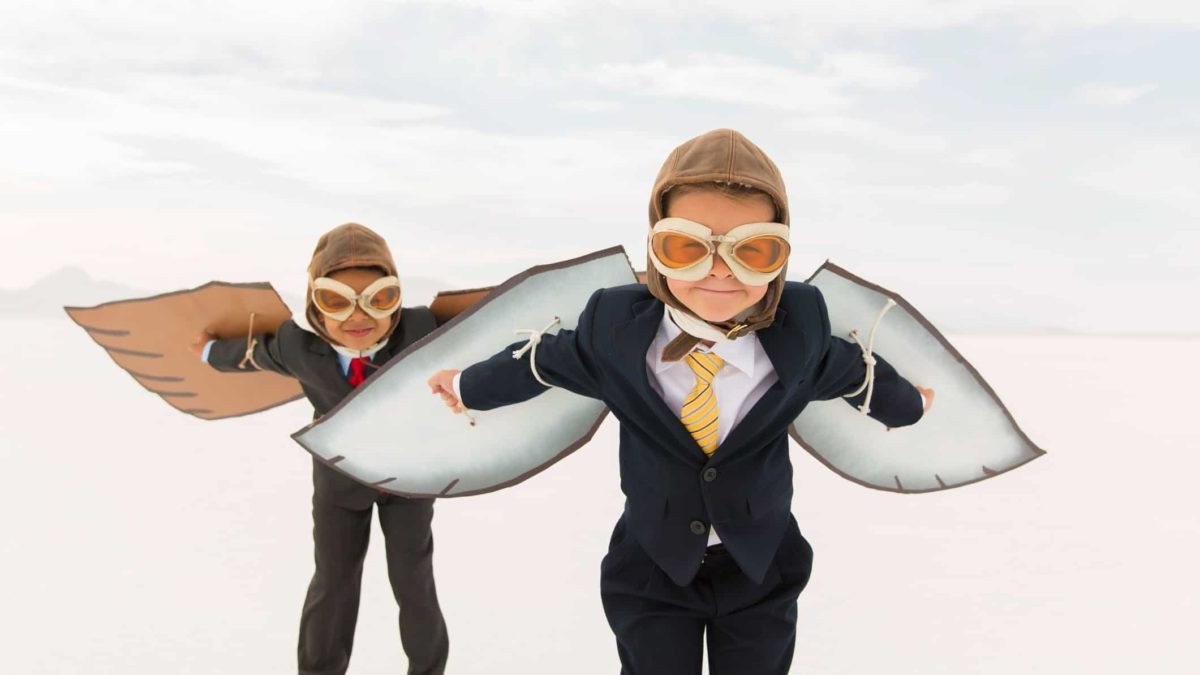Two young boys dressed in business buits with paper wings strapped on prepare for take-off