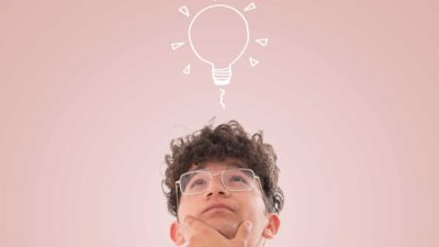 A youthful man looks up thoughtfully at a light bulb above his head.