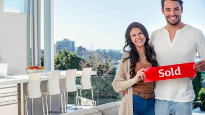 Happy couple holding red sold sticker inside their new apartment