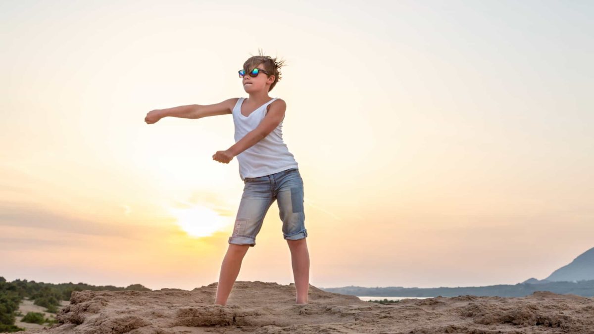 A teenage boy dances at sunset on the beach, moving his arms and hips to the beat.