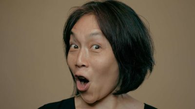 a woman raises her eyebrows and opens her mouth wide with a look of pleasant surprise.