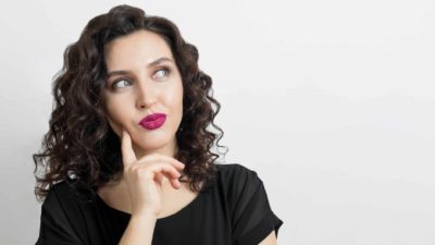 a woman holds her finger to the side of her face and looks upwards as she thinks about something.