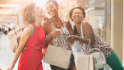 three happy shoppers pose together with their shopping bags thanks on a street.