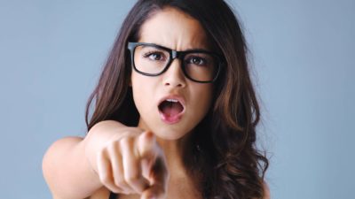 a woman with an aggrieved look on her face points a finger as if in admonishing someone.