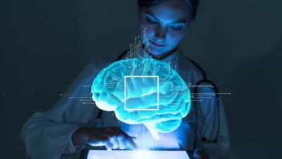 a scientist researcher operates a computer with a graphic image of a brain in the foreground signifying artificial intelligence or AI.