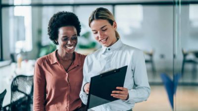 Two female executives looking at a clipboard together.