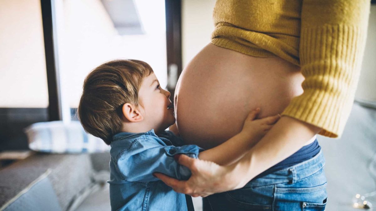 A little boy, soon to be a brother, kisses and holds his mum's pregnant tummy.