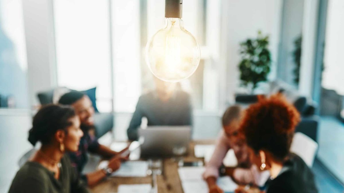 A light bulb sparks as it hangs over a meeting of members at the board table.