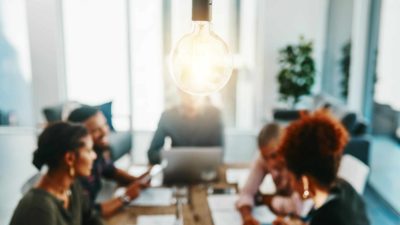 A light bulb sparks as it hangs over a meeting of members at the board table.