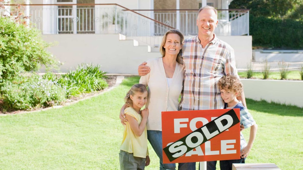 family stands together behind the sold for sale sign